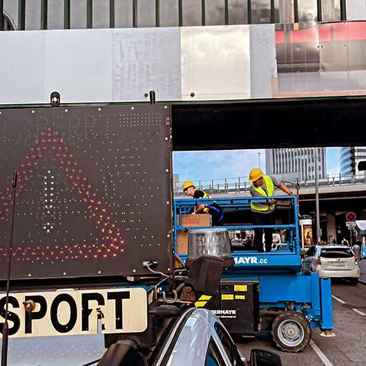 Branding Wiener Linien Steg: Arbeiter installieren Plakatwerbung in Wien Erdberg. Herausforderung im öffentlichen Raum.
