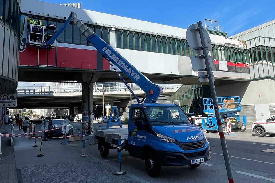 Wiener Linien Branding am Steg Wien Erdberg: Arbeiter an Hebebühne. Plakatives Design.