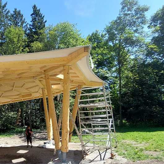 TechKonf: Holzkonstruktion im Bau. Gerüst und Baumaterialien sichtbar. Fokus auf Architektur und Design.