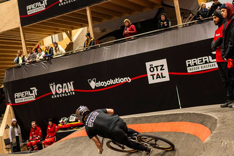 UCI Pump Track WM: Fahrer auf der Strecke im AREA47 Bikepark. Zuschauer und Sponsoren im Hintergrund.