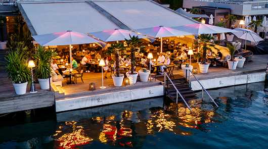 GLATZ Sonnenschirme: Restaurant am See mit Sonnenschirmen und Gästen.