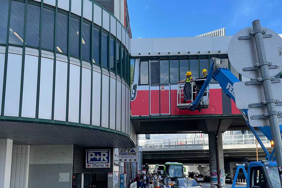 Branding Steg Wien Erdberg: Wiener Linien Straßenbahn-Branding am Steg, Arbeiter auf Hebebühne. Verkehr im Hintergrund.
