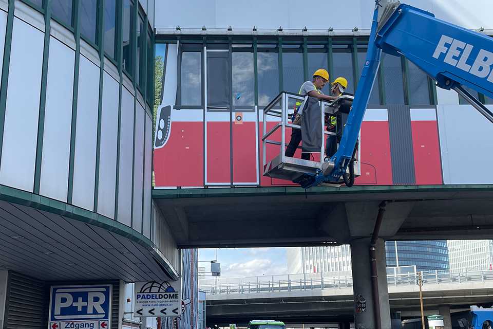 Branding Wiener Linien Steg Erdberg: Arbeiter montieren Plakat, U-Bahn-Motiv. Wien.